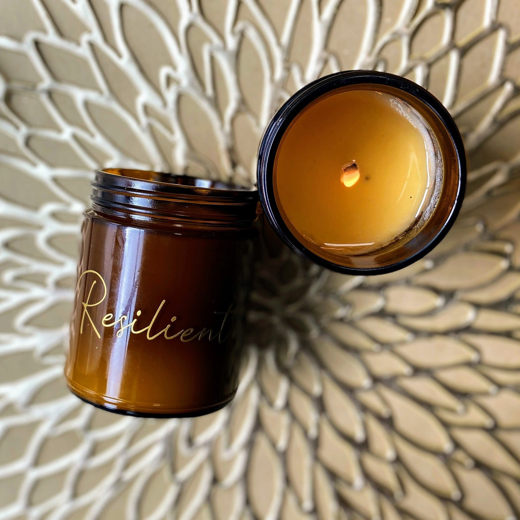 gold mat background amber glass jar candle lit flame resilient label on front of jar